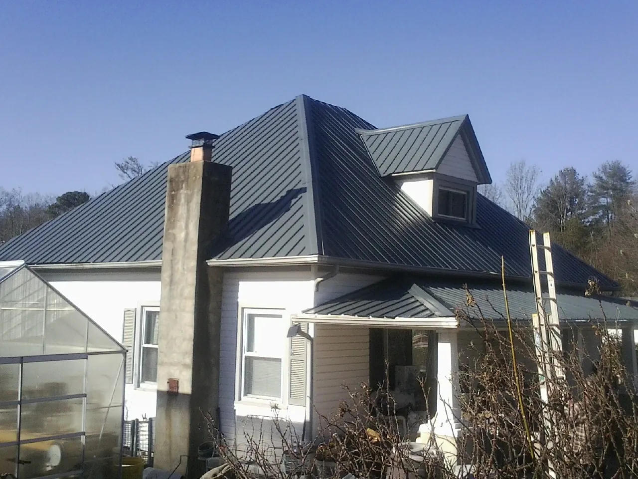Dark blue standing seam metal roof on a white farmhouse with dormer — Slate & Tile Roof Repair by Roofing Brothers in Columbus Junction