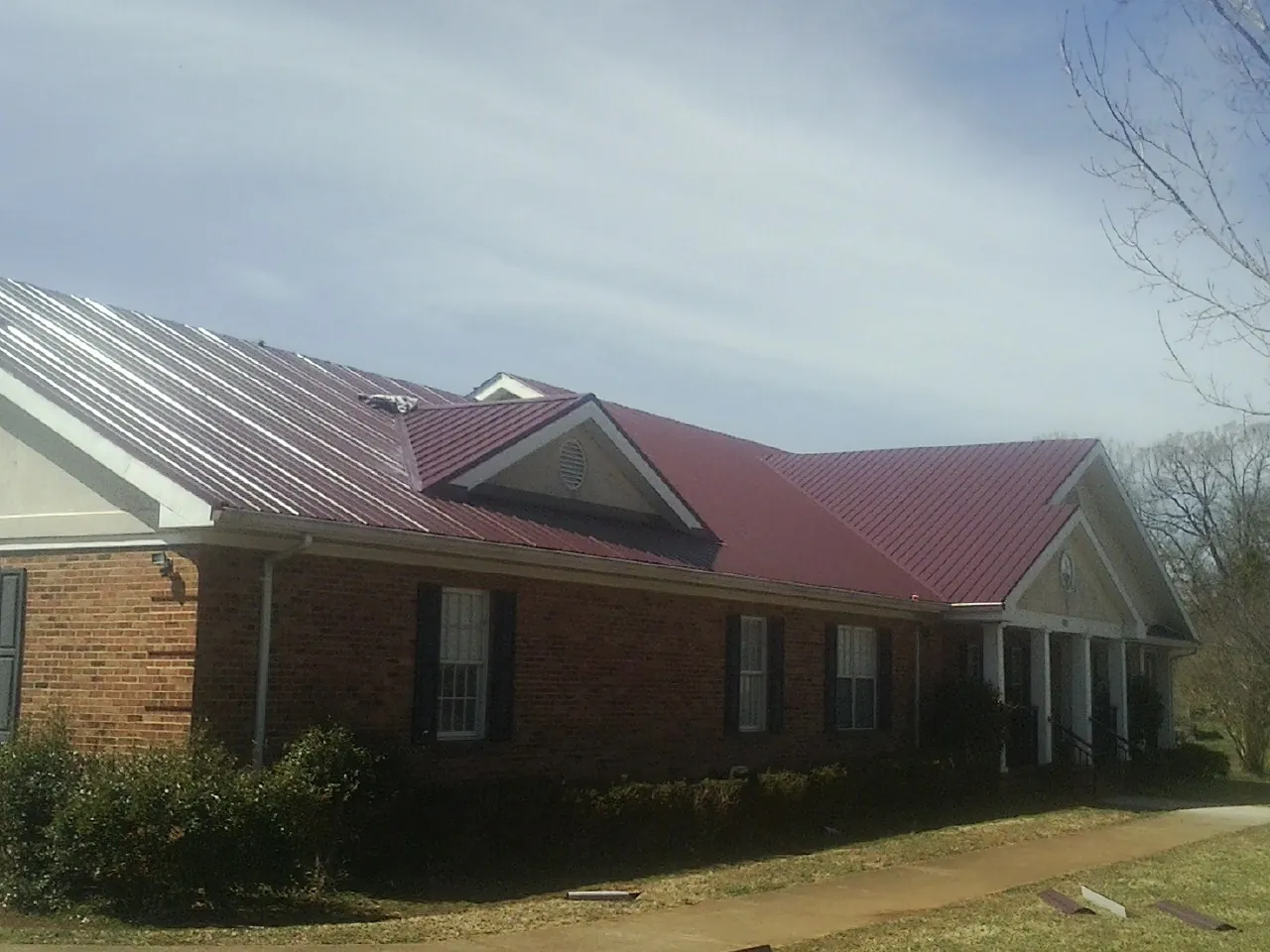 Red metal roof with gabled entries on a long brick building, from a Hail Damage Roof Repair job in Columbus Junction
