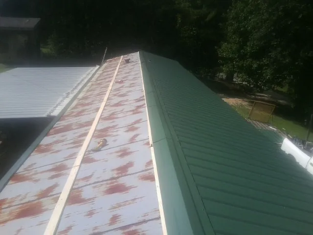 Old rusted panels beside newly installed green metal roofing — Wind Damage Roof Repair by Roofing Brothers in Columbus Junction