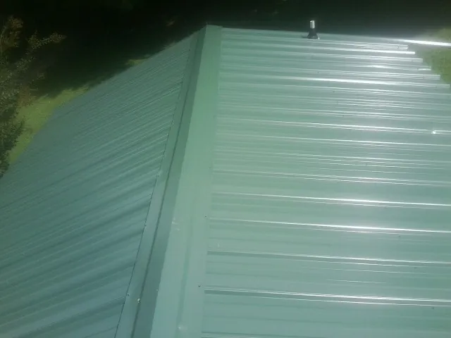 New green metal panels meeting at the ridge of a roof — Flat Roof Repair work by our crew in Columbus Junction