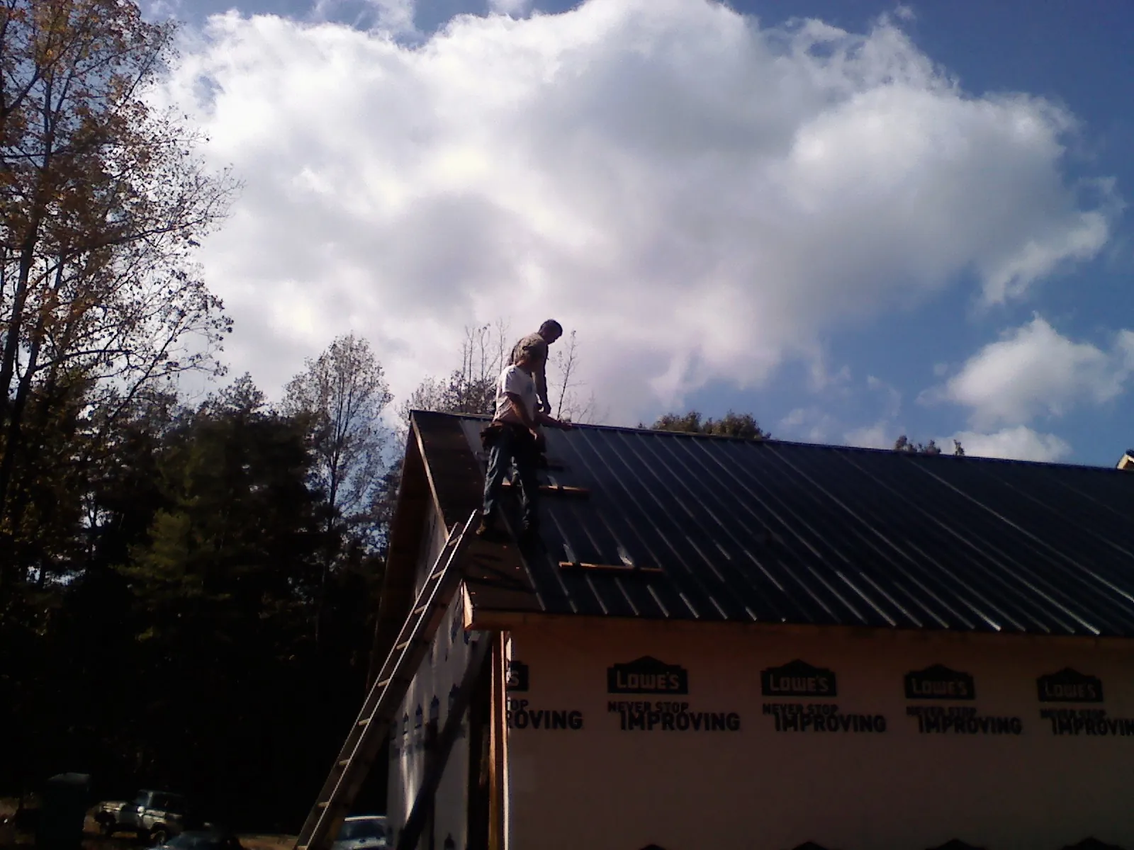 Roofer fastening dark metal panels high against a cloudy sky, from a Roof Inspection job in Columbus Junction