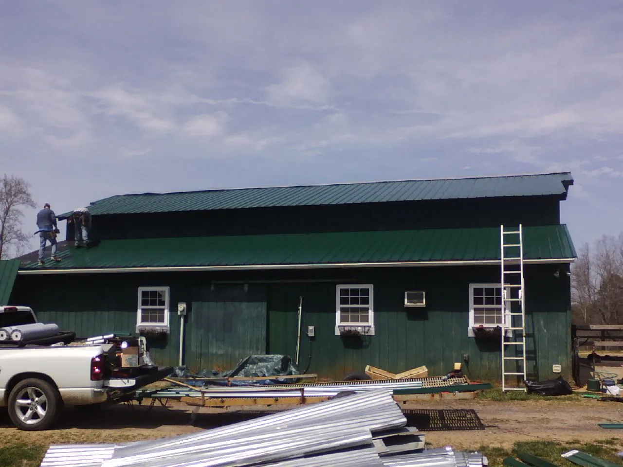 Crew installing green metal roofing on a large green barn in Columbus Junction