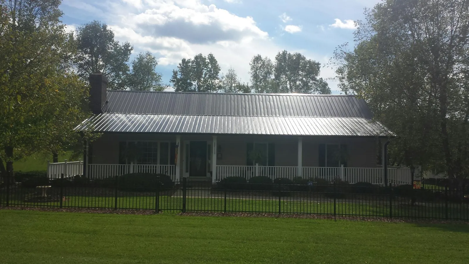Gray metal roof on a brick ranch with a full width front porch — Gutter Guard Installation work by our crew in Columbus Junction