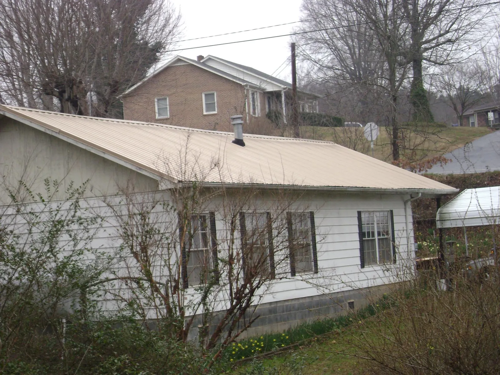 Tan metal roof on a white sided house set into a hillside — Commercial Roofing by Roofing Brothers in Columbus Junction