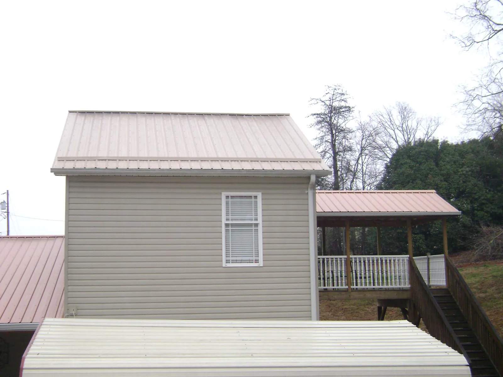 Tan metal roofs on a two story addition and attached porch, from a Roof Replacement job in Columbus Junction