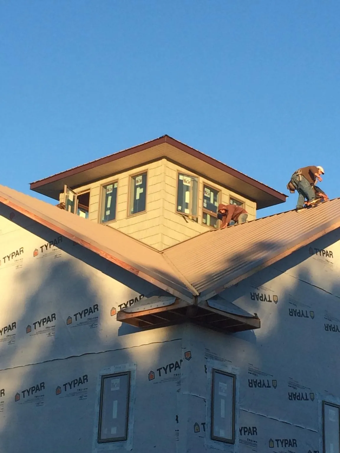 Roofers working around a rooftop cupola on a new metal roof at sunset — Roof Waterproofing in Columbus Junction by Roofing Brothers